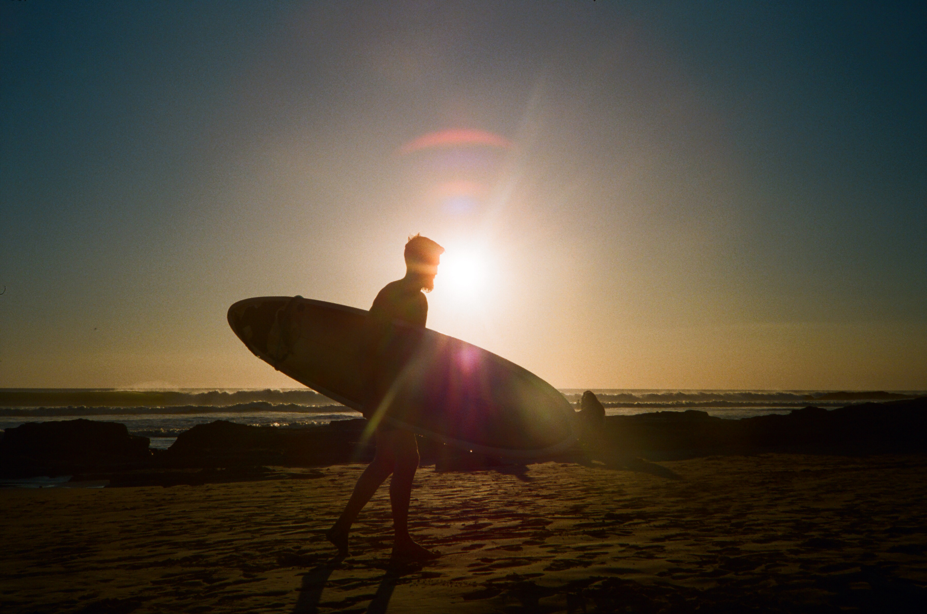 Silhouette of person with surfboard at sunset